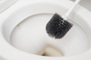 une femme au foyer est en utilisant une brosse à nettoyer le toilette photo