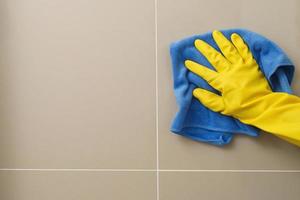 le femme au foyer est en utilisant une tissu à nettoyer le salle de bains mur. photo