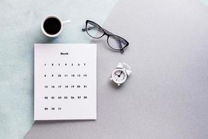 Vide feuille de mensuel calendrier, café tasse, alarme l'horloge et des lunettes sur texturé Contexte. temps Planification et organisation photo