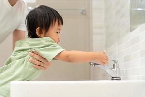 peu des gamins main fermé le robinet à évier dans maison avec maman. mère enseigne enfant à enregistrer l'eau. garde tournant de le l'eau à enregistrer monde énergie et protéger le environnement, monde l'eau journée photo