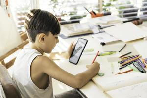une garçon est apprentissage à dessiner avec sa intelligent téléphone. photo