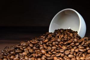 Grain de café sortant d'une tasse blanche sur table en bois photo