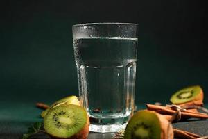 une verre de du froid l'eau sur une vert Contexte. décoré avec tranche kiwi, cannelle des bâtons, Badyan, menthe feuilles. copie espace photo