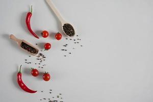 Cerise tomates, rouge chaud le Chili poivre, parfumé noir poivre pois sur une blanc Contexte. Contexte avec épices. plat poser, copie espace photo