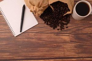 café, grains de café et un cahier avec un stylo sur un bureau en bois photo