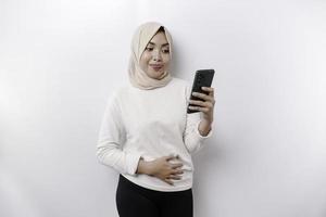 une réfléchi Jeune asiatique musulman femme portant une hijab et en portant sa menton tandis que parlant sur le téléphone isolé par une blanc Contexte photo