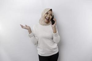 femme asiatique excitée portant le hijab pointant vers l'espace de copie à côté d'elle tout en tenant son téléphone, isolée sur fond blanc photo