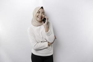 une content asiatique musulman femme portant une foulard, en portant sa téléphone, isolé par blanc Contexte photo