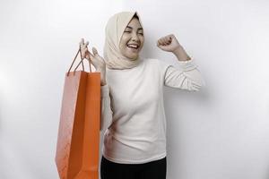 asiatique musulman femme content magnifique Jeune permanent excité en portant une achats sac, studio coup isolé sur blanc Contexte photo