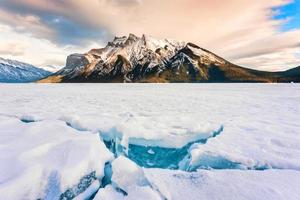 congelé Lac minnewanka avec rocheux montagnes et fissuré la glace de le Lac dans hiver à banff nationale parc photo
