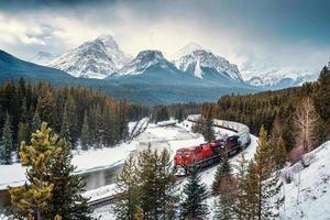 morants courbe avec iconique rouge cargaison train qui passe par arc vallée et rocheux montagnes dans hiver à banff nationale parc photo