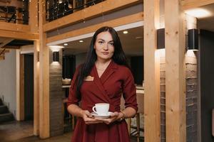 Une femme gérante de restaurant porte un masque noir et des gants jetables tenant une tasse de café dans un restaurant photo