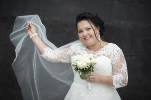 portrait de une plein la mariée avec une agitant voile avec une bouquet sur une foncé Contexte. photo