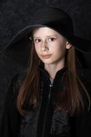 portrait de une peu fille dans une noir chapeau sur une foncé Contexte. photo