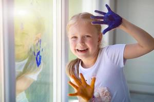 les enfants fille dessiner avec paumes sur le la fenêtre. peint mains laisser une marque sur le verre. quarantaine. rester maison. photo