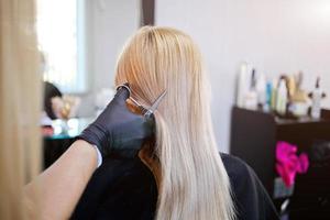 coiffeur avec Sécurité les mesures pour COVID-19 [feminine, une femme dans une médical masque, social distance, Coupe cheveux avec une médical masque et caoutchouc gants dans une beauté salon. photo