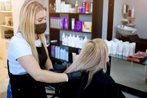 coiffeur avec Sécurité les mesures pour COVID-19 [feminine, une femme dans une médical masque, social distance, Coupe cheveux avec une médical masque et caoutchouc gants dans une beauté salon. photo