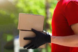 livraison homme dans rouge uniforme en portant papier carton des boites dans médical caoutchouc gants à le coucher du soleil sur Extérieur. vite et gratuit livraison transport . photo