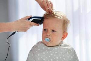 mère Coupe le cheveux de une peu fils. photo