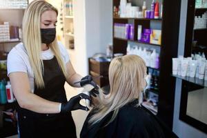 une coiffeur dans médical masque et caoutchouc gants détient une paire de les ciseaux et une peigne. coiffure salon ouvert. photo