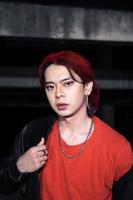 un asiatique homme avec rouge cheveux et une noir veste est posant dans un abandonné bâtiment photo