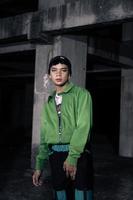 un asiatique homme sourit tandis que portant une vert parachute veste et noir un pantalon photo