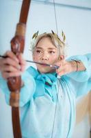 un asiatique femme avec blond cheveux en portant un La Flèche tandis que portant une bleu robe photo