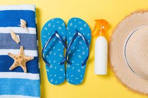 tongs, chapeau de paille, étoile de mer, bouteille de crème solaire, spray de lotion pour le corps sur fond jaune vue de dessus. fond d'accessoires de mer de plage d'été à plat, concept de voyage photo