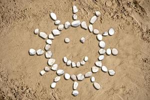 Soleil avec une sourire fabriqué avec des pierres sur le sable photo