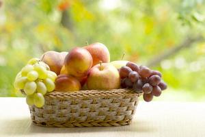 Frais mûr pommes, les pêches, vert et bleu les raisins dans panier. en bonne santé nourriture sur table sur défocalisation l'automne Contexte. photo