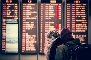 malheureux et stressé Jeune adulte couple à aéroport visualisation annulé vols sur vol information et aéroport afficher planche - génératif ai. photo