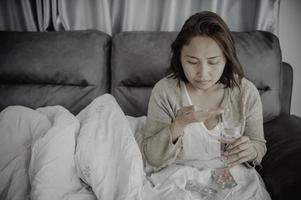 une femme malade asiatique s'assoit sur le canapé reste à la maison, la femme se sentait mal, voulait s'allonger et se reposer, forte fièvre photo