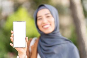 musulman femme montrant le écran de une mobile en plein air photo