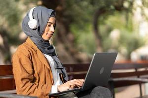 musulman femme en utilisant une portable tandis que séance sur une parc photo