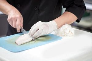 concentré Masculin chef dans uniforme Coupe poisson filet sur conseil, chef coupes blanc tilapia poisson dans cuisine. photo
