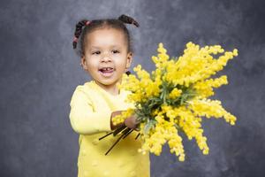 peu africain américain fille avec Jaune fleurs sur une gris Contexte. photo