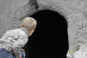le enfant regards dans le noir trou de le grotte. le concept de apprentissage le inconnu. puéril curiosité. photo