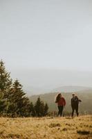 Couple souriant marchant avec des sacs à dos sur les collines verdoyantes photo