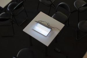 Haut vue de une portable entouré par Bureau chaises.lumineux portable sur une foncé Contexte. photo