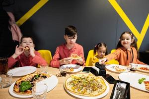 quatre des gamins en mangeant italien Pizza dans pizzeria. les enfants manger à café. photo