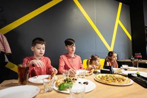 quatre des gamins en mangeant italien Pizza dans pizzeria. les enfants manger à café. photo