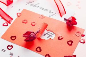 la Saint-Valentin journée. le Date février 14 est Souligné avec une trou dans rouge papier carton, séché fleurs et une ruban sur une rose Contexte photo