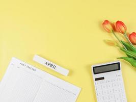 plat disposition de habitude traqueur livre, blanc calculatrice, en bois calendrier avril et tulipes sur Jaune Contexte. photo