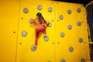 peu fille enfant escalade mur à Jaune terrain de jeux parc. enfant dans mouvement pendant actif divertissements. photo