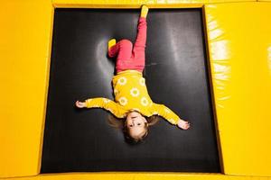 bébé fille enfant mensonges à l'envers vers le bas sur trampoline à terrain de jeux parc. enfant dans mouvement pendant actif divertissements. photo