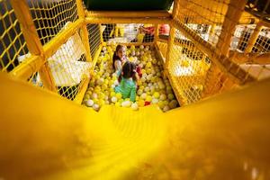 Fratrie jouer avec coloré des balles à Jaune terrain de jeux parc. sœurs dans actif divertissements. photo