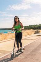 femme équitation électrique scooter, content et été balade à tropical île plage recours pour vacances. ville, rue et éco amical transport, amusement sur escooter sur vacances dans Majorque, baléares île photo