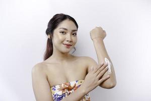 peau se soucier des produits concept. asiatique femme appliquant hydratant lotion sur corps après douche, permanent enveloppé dans serviette, tondu image photo