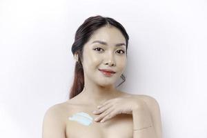 peau se soucier des produits concept. asiatique femme appliquant hydratant lotion sur corps après douche, permanent enveloppé dans serviette, tondu image photo