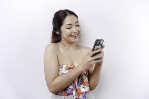 une portrait de une content asiatique femme en portant sa téléphone, isolé par blanc Contexte photo